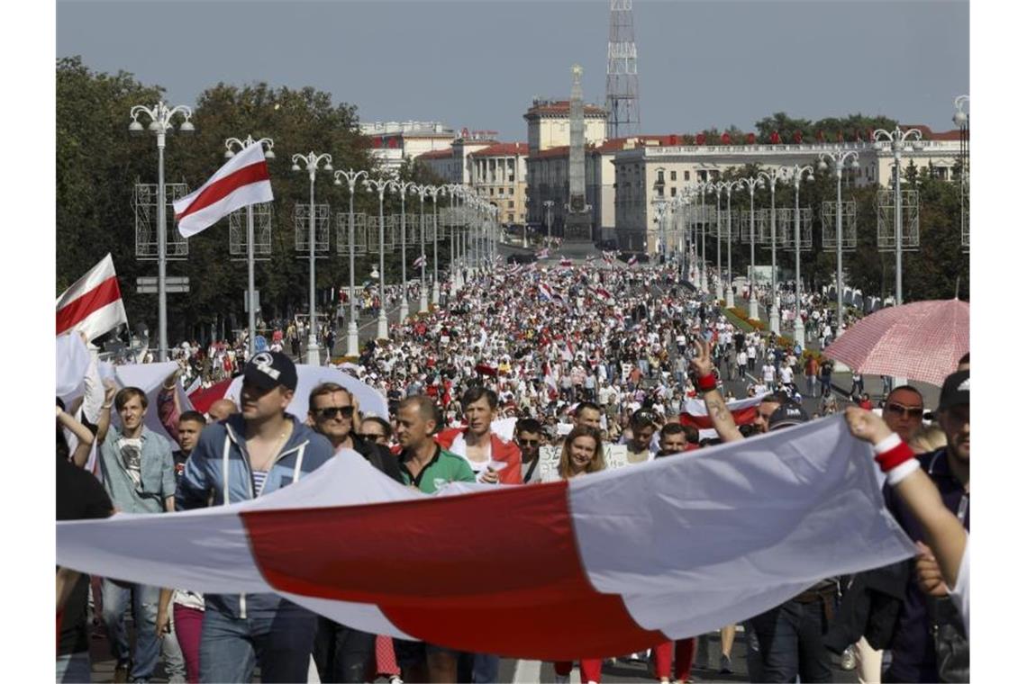 Demonstranten marschieren mit der ehemaligen belarussischen Nationalflagge in den Händen auf der Straße. Foto: Uncredited/AP/dpa