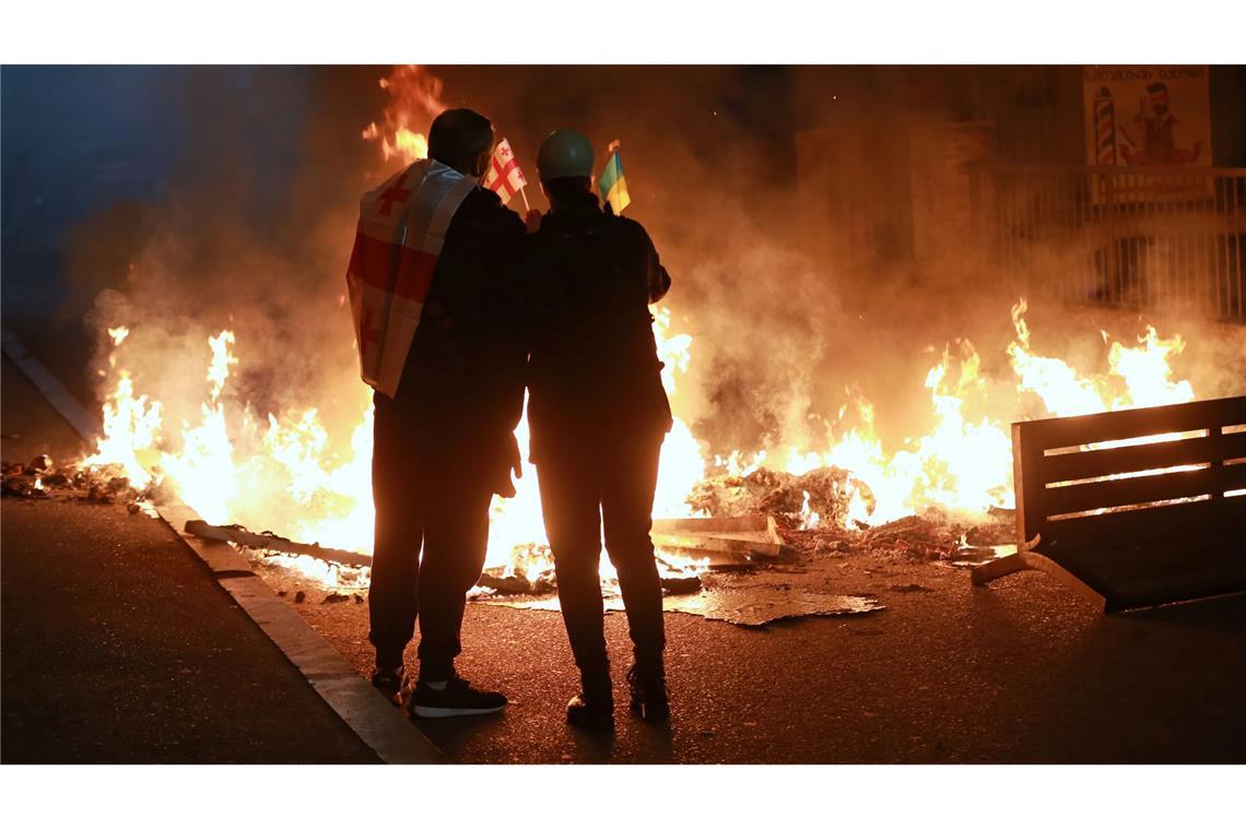 Demonstranten mit einer georgischen und einer ukrainischen Nationalflagge stehen im Stadtzentrum von Tiflis hinter einer brennenden Barrikade während einer Kundgebung der Opposition, bei der sie die Kommunalwahlen boykottieren und die Freilassung politischer Gegner fordern.