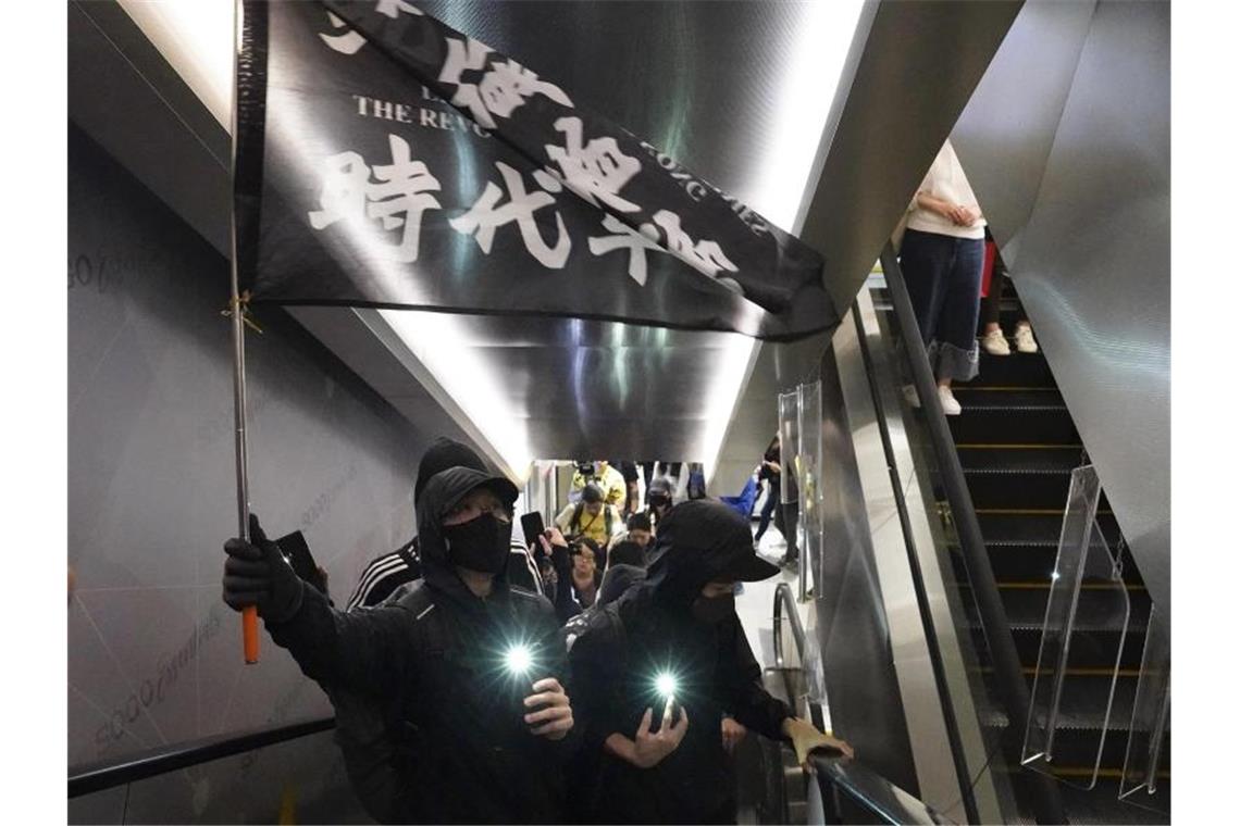 Demonstranten mit Mundschutz tragen eine Flagge mit der Aufschrift „Befreit Hongkong, die Revolution unserer Zeit“ in einem Einkaufszentrum. Foto: Vincent Yu/AP/dpa