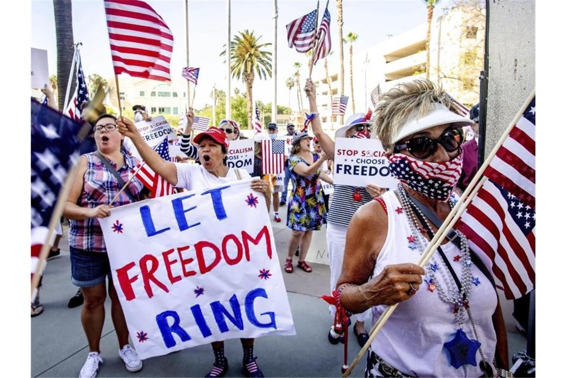 Demonstranten protestieren mit amerikanischen Flaggen und Plakaten gegen die Aufhebungen von Beschränkungen, die zur Eindämmung der Corona-Pandemie, eingeführt wurden. Foto: Watchara Phomicinda/The Orange County Register/AP/dpa