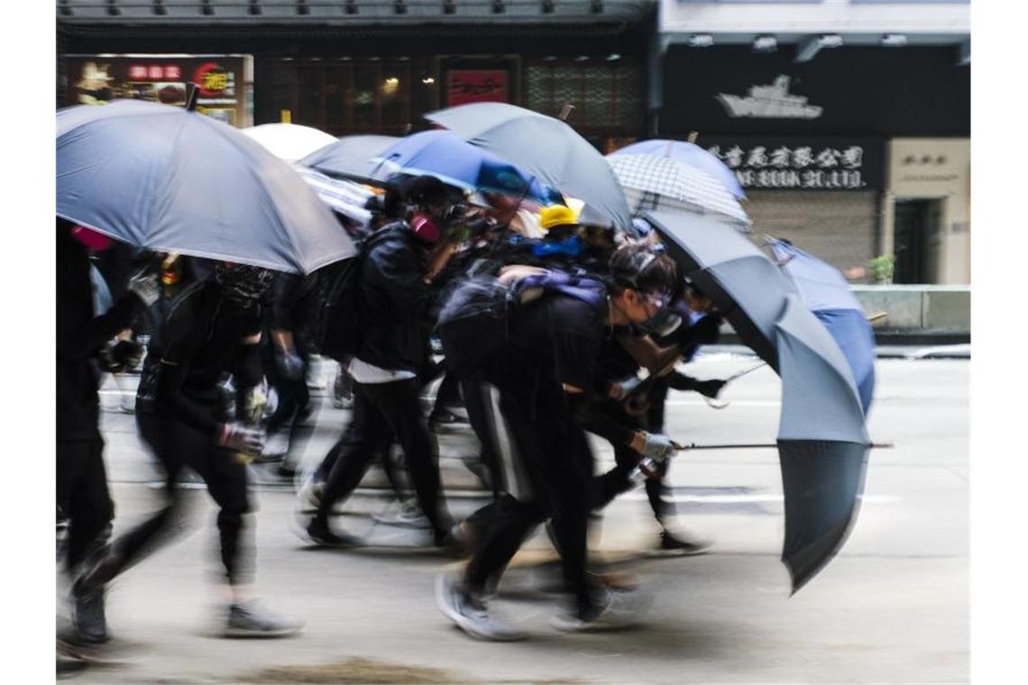 Demonstranten schützen sich auf einer Straße mit Regenschirmen. Foto: Keith Tsuji/SOPA Images via ZUMA Wire/dpa