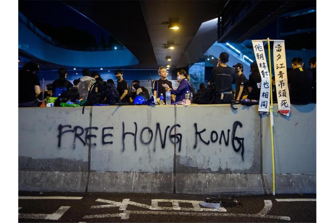 Demonstranten sitzen auf einer Mauer, die mit einem Grafitti („Free Hong Kong“) beschrieben wurde. Foto: Gregor Fischer/dpa/Archiv