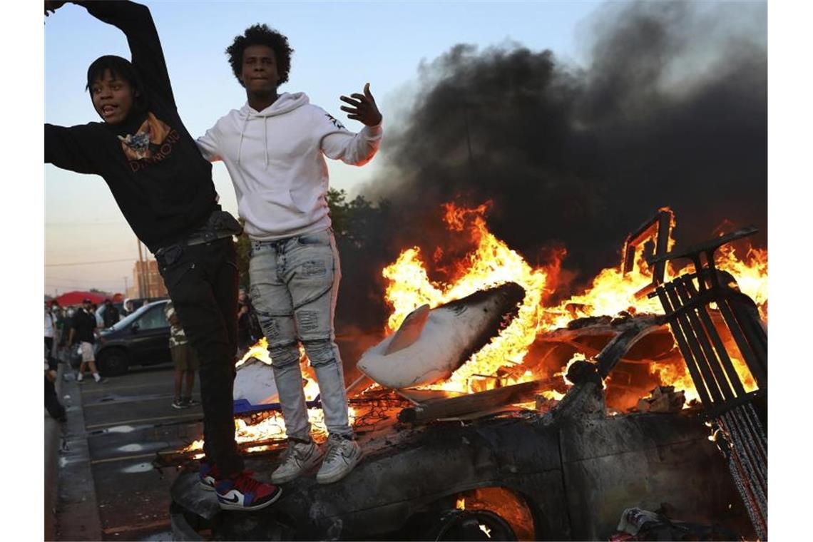 Demonstranten stehen auf einem brennenden Auto. Foto: David Joles/Star Tribune/AP/dpa