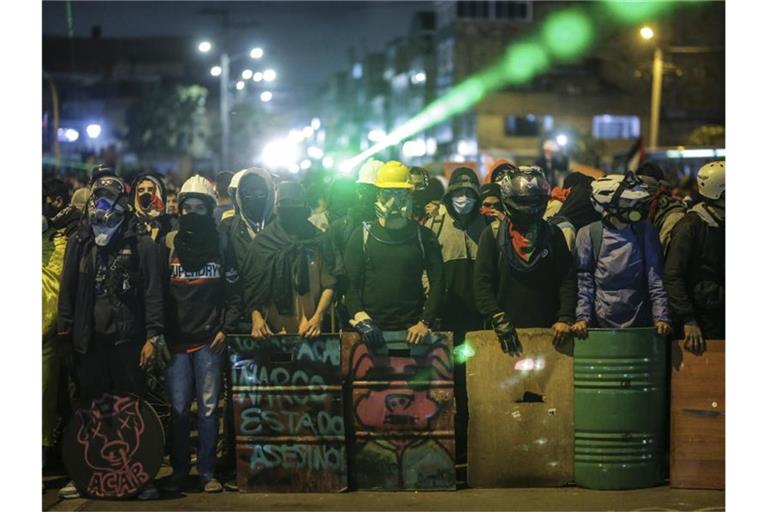 Demonstranten stehen bei einem Protest an einer Kreuzung mit Schildern und Laserpointern. Foto: Ivan Valencia/AP/dpa