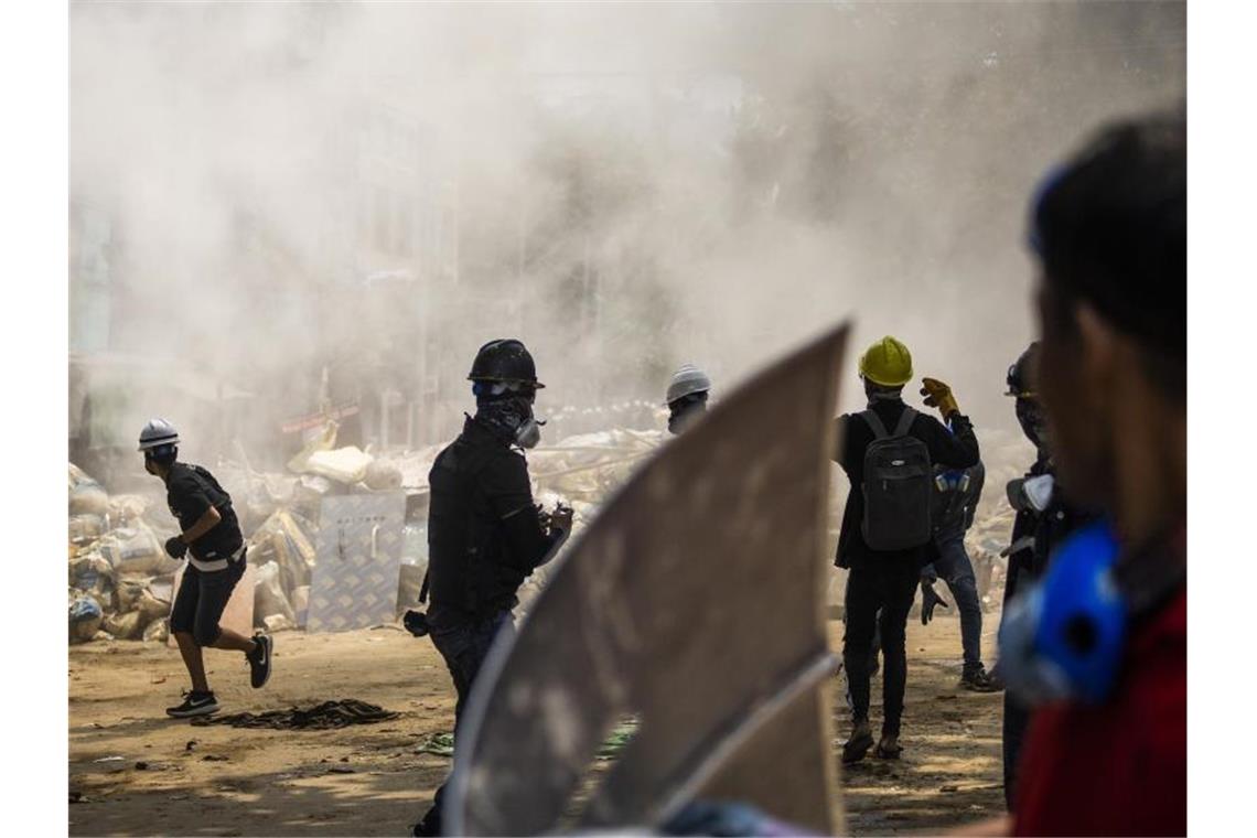 Demonstranten stehen vor rauchenden Trümmern einer provisorischen Barrikade bei einem Anti-Putsch-Protest in Yangon. Myanmarische Sicherheitskräfte haben heute erneut Waffengewalt gegen eine Demonstration gegen die Militärjunta eingesetzt. Foto: Uncredited/AP/dpa