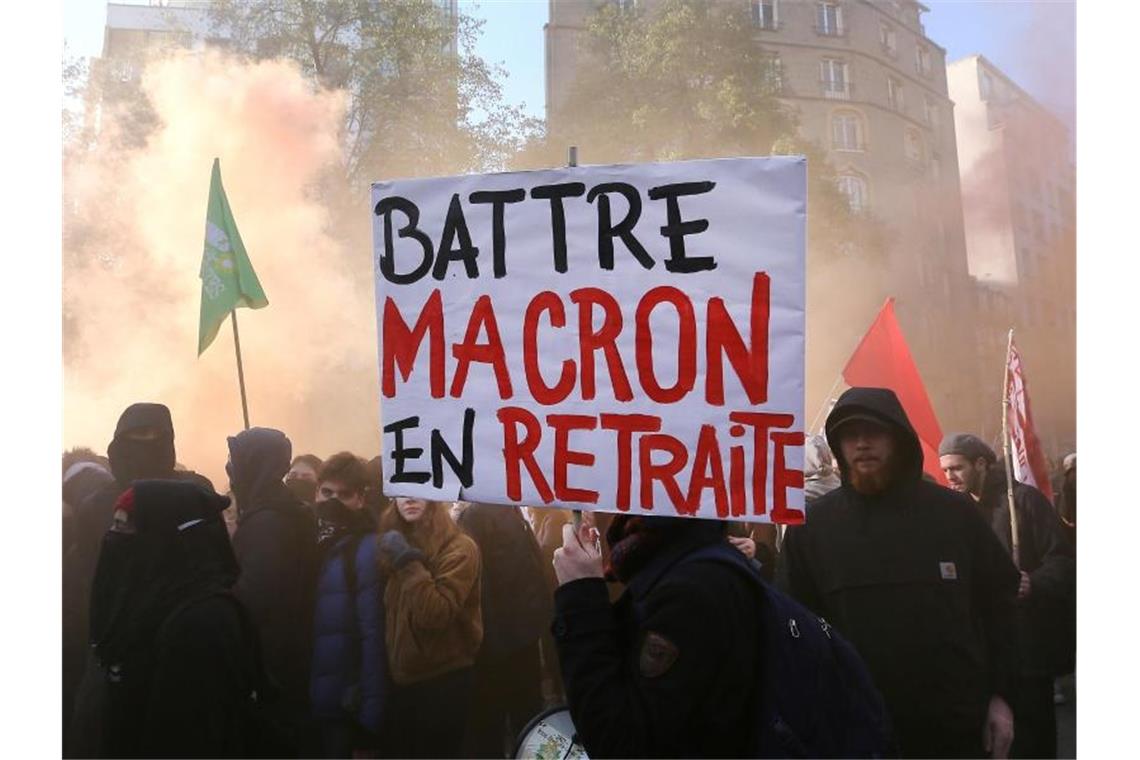 Demonstranten tragen ein Plakat mit der Aufschrift „Battre Macron en Retraite“ (sinngemäß: „Macron zum Rücktritt zwingen“). Foto: David Vincent/AP/dpa