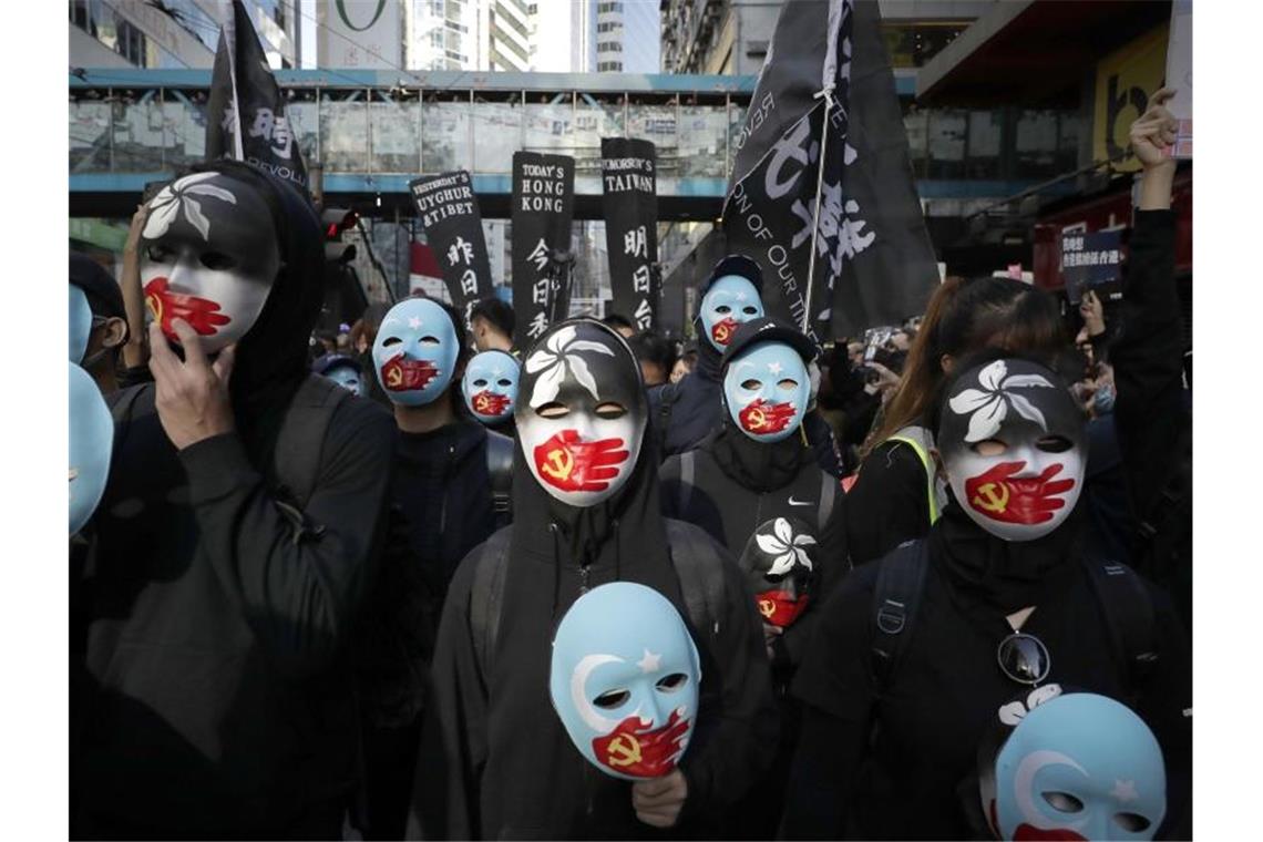 Demonstranten tragen Masken, auf denen eine rote Hand mit chinesischer Flagge den Mund zuhält. Foto: Mark Schiefelbein/AP/dpa