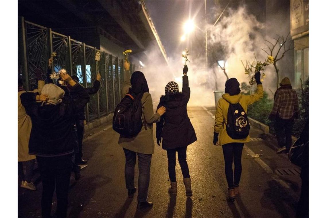 Demonstrantinnen erinnern mit weißen Blumen an die Opfer des Flugzeugabschusses, während Sicherheitskräfte Tränengas in ihre Richtung schießen. Foto: AP/dpa