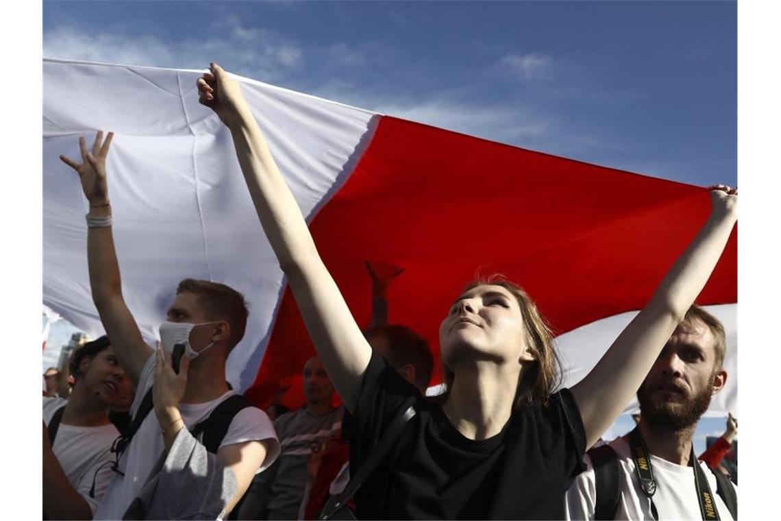 Demonstrantinnen und Demonstranten halten eine historische belarussische Flagge und nehmen an einem Protest der Opposition in Minsk teil. Foto: -/AP/dpa