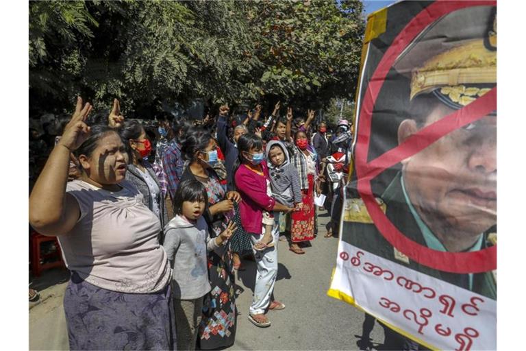 Demonstrantinnen zeigen den Dreifinger-Gruß, ein Symbol des Widerstandes, während eines Protestes gegen den Militärputsch in Myanmar. Daneben ein Plakat mit einem durchkreuzten Porträt von General Min Aung Hlaing. Foto: Str/AP/dpa