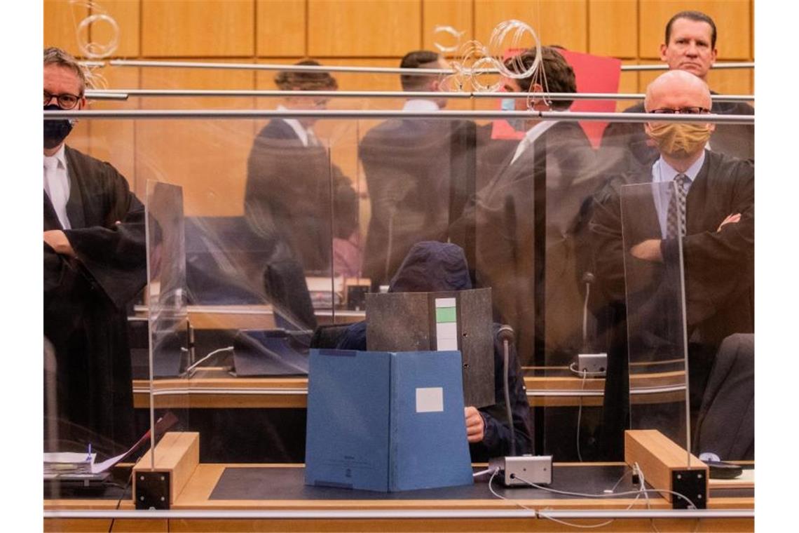 Prozessstart im Missbrauchsfall Münster Der 27-Jährige Hauptangeklagte (vorne), seine Mutter (ganz hinten links) und ein dritter Angeklagter (roter Hefter) sitzen in einem Gerichtssaal des Landgerichts. Foto: Rolf Vennenbernd/dpa-Pool/dpa