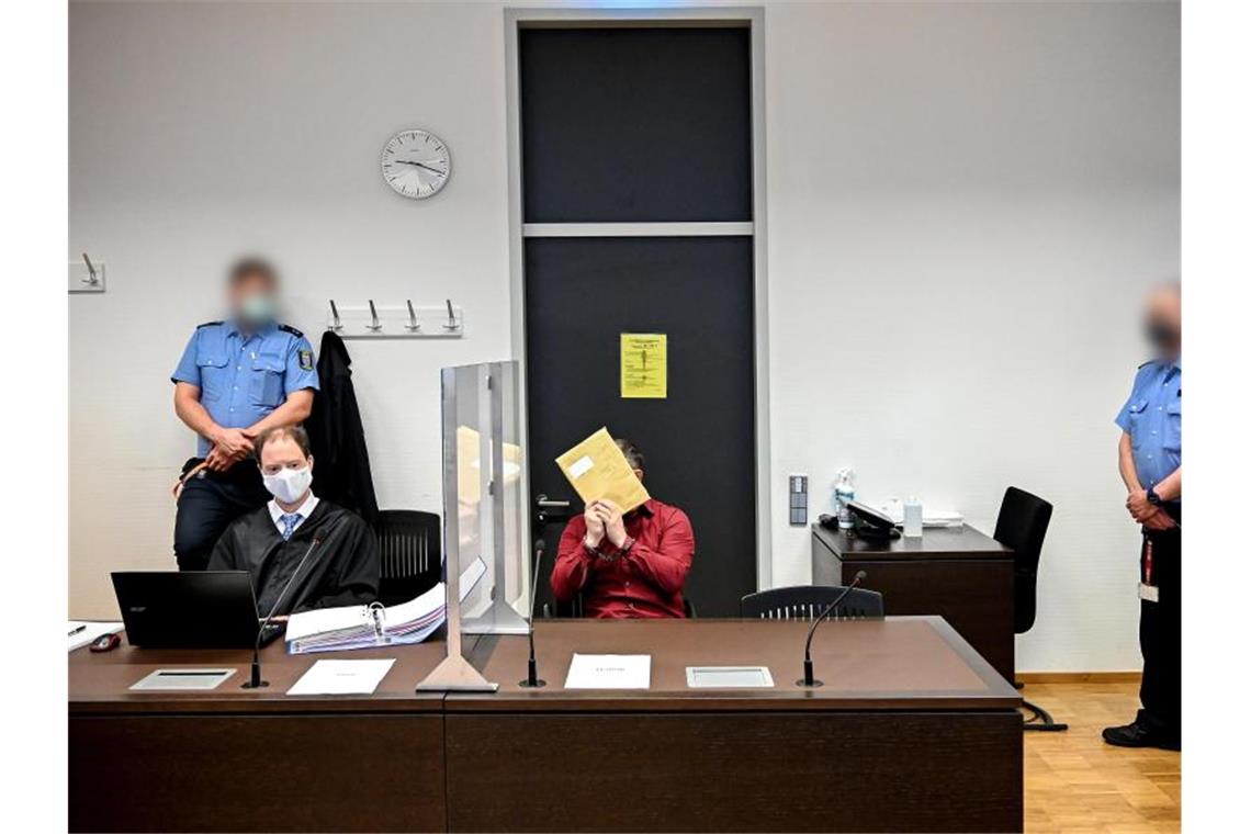 Der Angeklagte (M) sitzt in Handschellen im Gerichtssaal des Landgerichts neben seinem Anwalt, und verbirgt sein Gesicht. Foto: Sascha Steinbach/epa/Pool/dpa