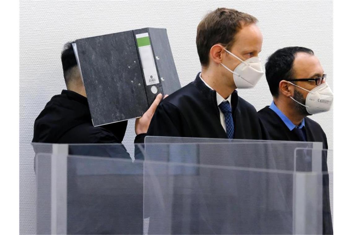 Der Angeklagte verbirgt im Sitzungssaal des Landgerichts Ingolstadt sein Gesicht hinter einem Aktenordner. Davor stehen seine Verteidiger. Foto: Ulf Vogler/dpa/Archiv