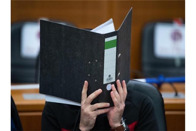 Der Angeklagte verbirgt sein Gesicht hinter einem Aktendeckel. Foto: Boris Roessler/dpa