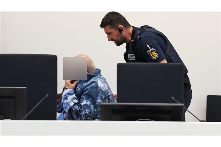 Der Angeklagte wird von einem Justizmitarbeiter in den Verhandlungssaal gefahren, er sitzt im Rollstuhl.