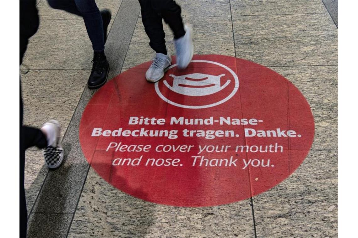 Der Aufkleber "Bitte Mund-Nase-Bedeckung tragen. Danke" ist im Bahnhof am Alexanderplatz in Berlin auf dem Boden befestigt. Foto: Paul Zinken/dpa