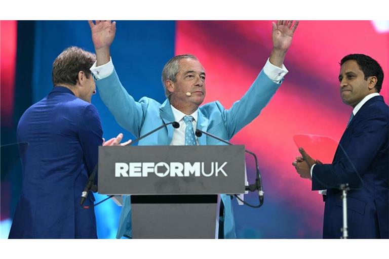 Der Chef der Reform UK Partei, Nigel Farage, wird nach seiner Rede auf dem Parteitag in Birmingham gefeiert. Auf der Bühne spenden ihm der stellvertretende Vorsitzende Richard Tice (L) und der Schatten-Innenminister Zia Yusuf Beifall.