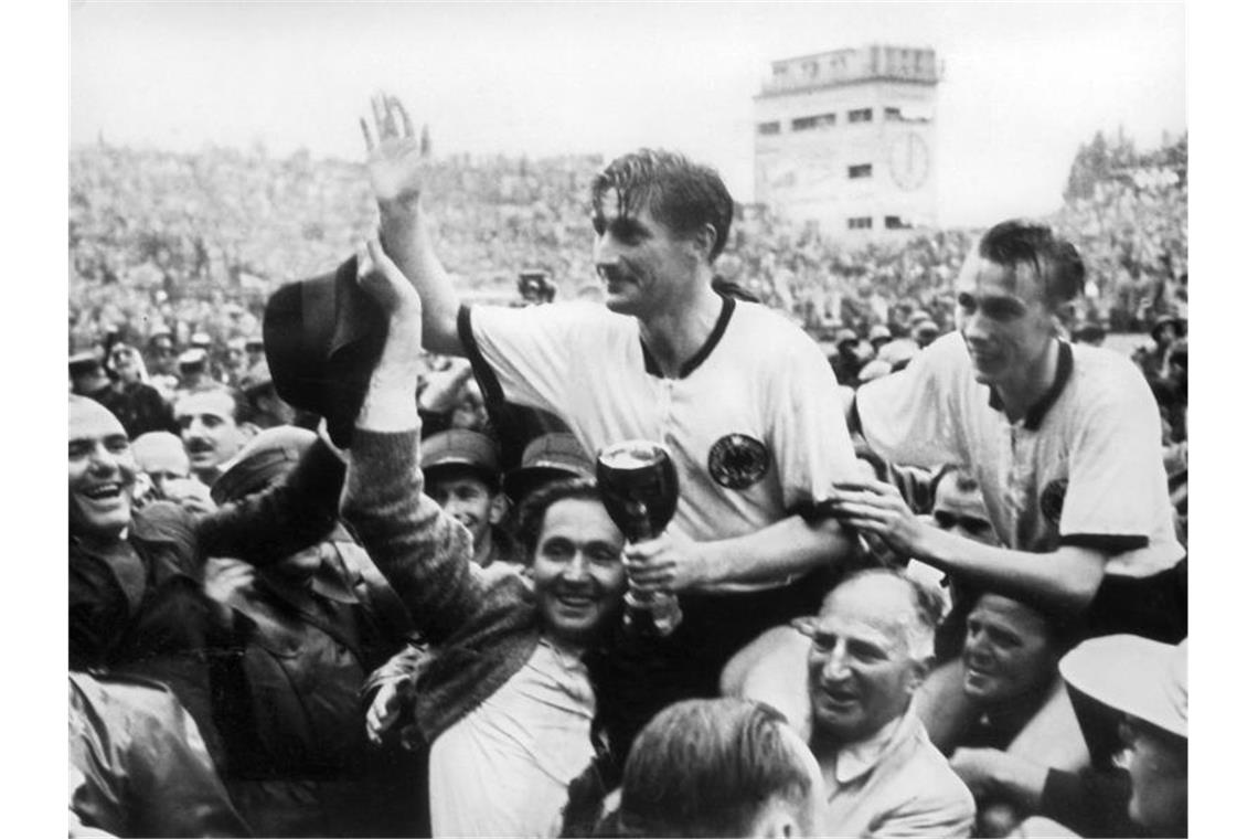 Der deutsche Stürmer und Kapitän Fritz Walter (M, oben) und sein Lauterer Teamgefährte Horst Eckel (r) werden nach dem Triumph im Fußball-WM-Finale im Berner Wankdorfstadion von begeisterten Anhängern vom Spielfeld getragen. Foto: picture alliance/dpa/Archivbild