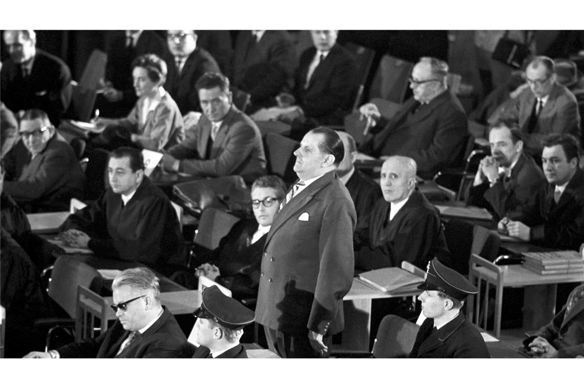 Der erste Auschwitz-Prozess im Plenarsaal der Frankfurter Stadtverordnetenversammlung wird eröffnet. In der ersten Reihe sitzt der Angeklagte Victor Capesius (mit dunkler Brille), hinter ihm steht der Angeklagte Oswald Kaduk. (zu dpa: "Als die Täter von Auschwitz in Frankfurt vor Gericht kamen")