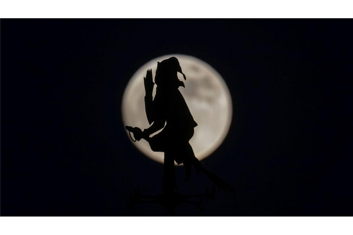 Bilder des Tages Der fast vollständige Mond steht hinter einer Wetterfahne in Form von einer auf einem Besen reitenden Hexe.