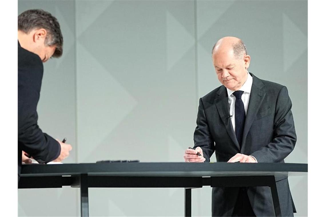 Der Grünen-Vorsitzende Robert Habeck (l) und der neue Kanzler Olaf Scholz (SPD) setzen ihre Unterschriften unter das Dokument. Foto: Michael Kappeler/dpa