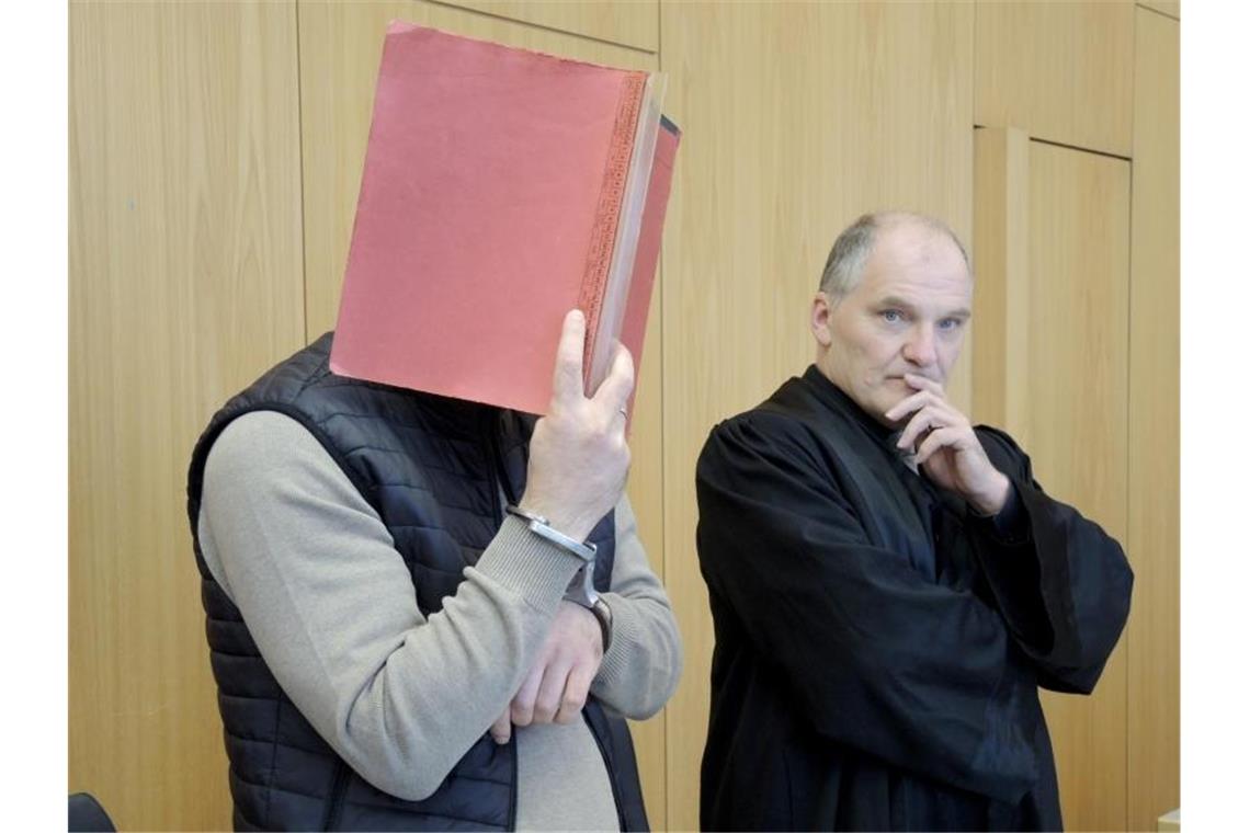 Der Hauptangeklagte (l) steht vor dem Beginn der Urteilsverkündung mit einem Aktendeckel seinem Gesicht. Foto: Thomas Burmeister