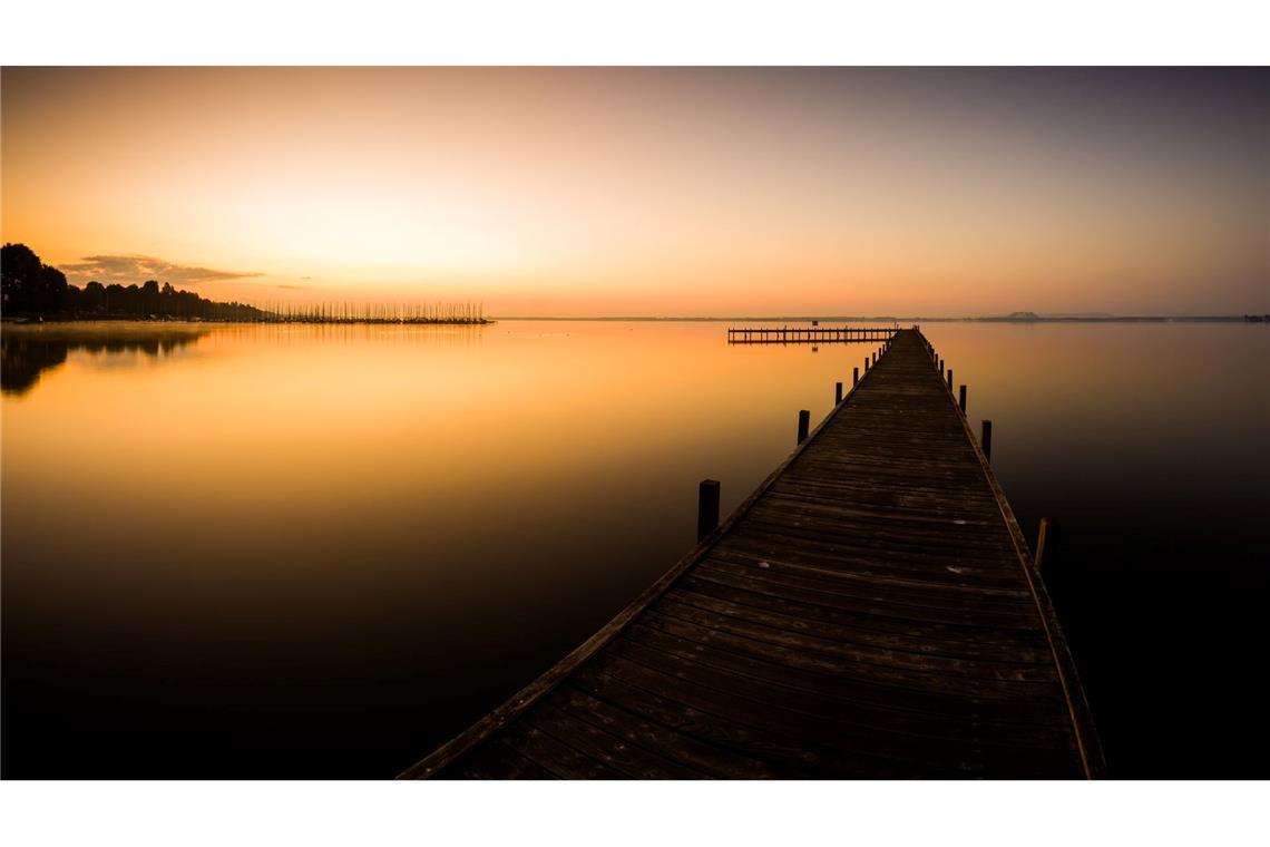 Der Himmel über einem Steg am Steinhuder Meer in der Region Hannover ist bei Sonnenaufgang orange.