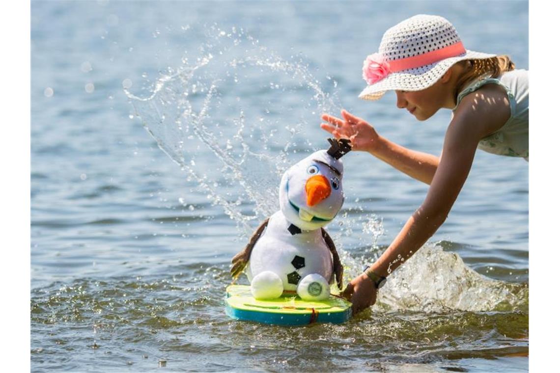 Der kann's besonders gut brauchen: Die kleine Lilith erfrischt ihren Stoff-Schneemann Olaf, Figur aus dem Disney-Film „Die Schneekönigin“, mit Wasser aus dem Main bei Flörsheim. Foto: Andreas Arnold