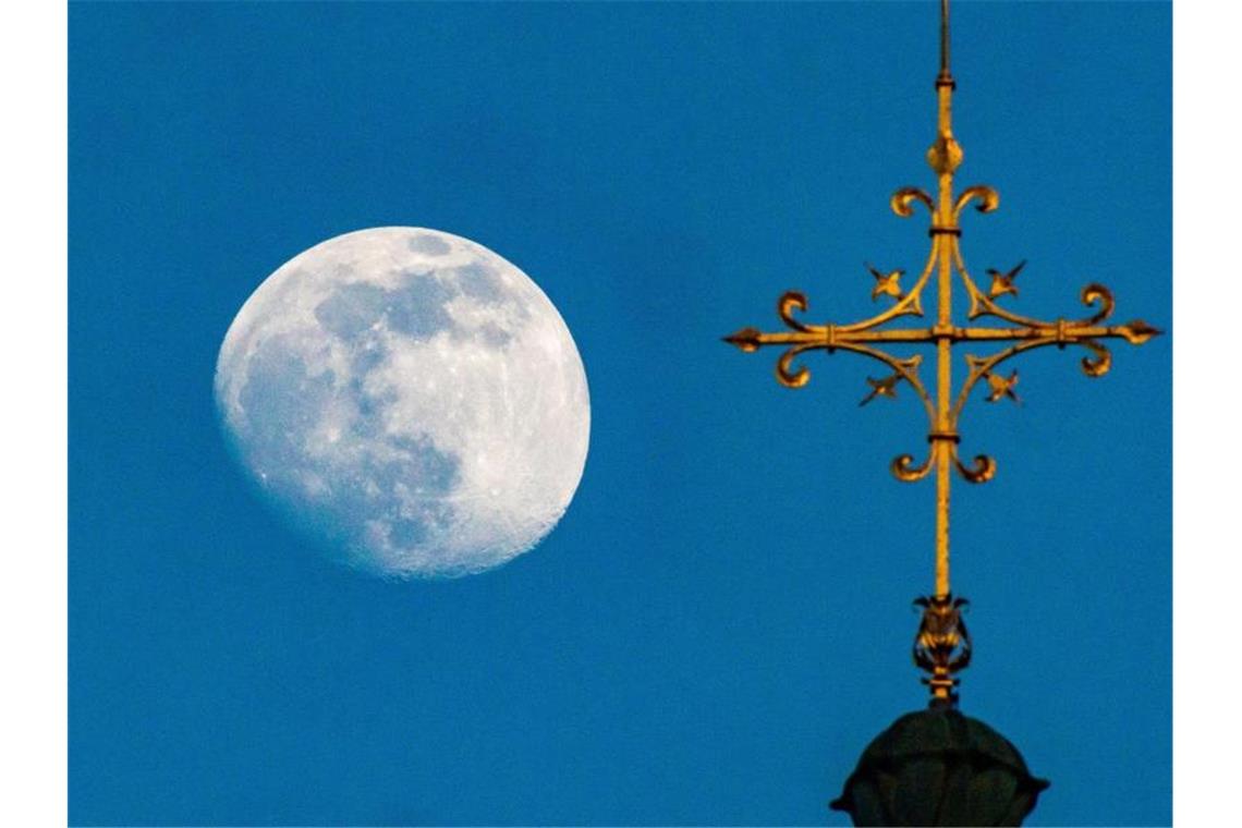 Der Mond zieht an einem an einem Kreuz eienr Kirche vorbei. Foto: Peter Kneffel/dpa/Archivbild