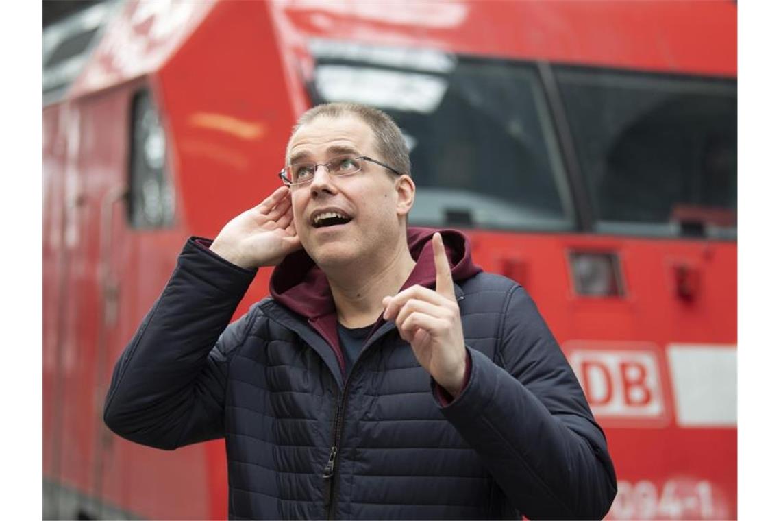 Der neue Bahnsansager Heiko Grauel steht an einem Bahnhof vor einem Zug. Foto: Boris Roessler/dpa/Archivbild