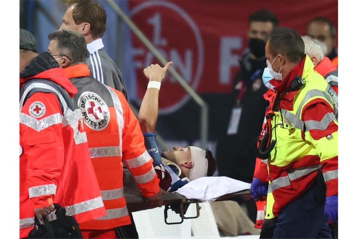 Krauß gibt nach Kopftreffer Entwarnung: „Mir geht es gut“ Der Nürnberger Tom Krauß (M) wird verletzt aus dem Stadion getragen, zeigt aber mit dem Daumen nach oben. Foto: Daniel Karmann/dpa