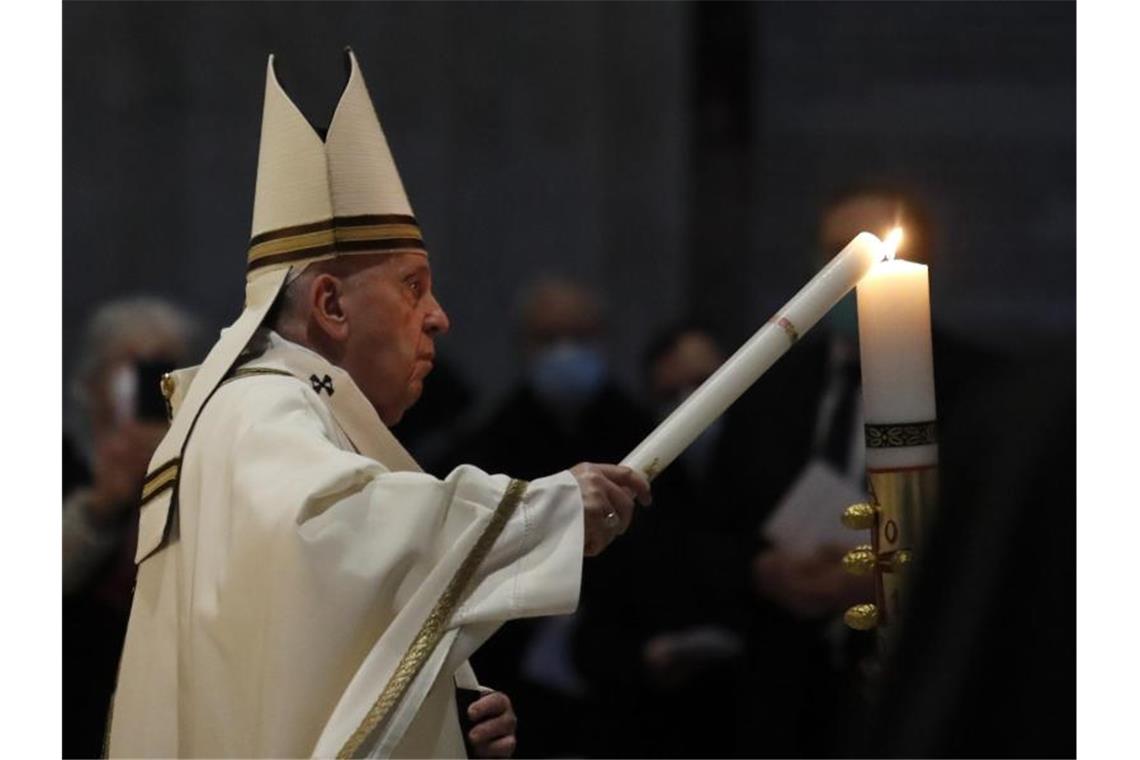 Oster-Appell: Weniger Waffen und mehr Impfungen Der Pontifex trägt die Osterkerze - das Licht Christi - in den dunklen Petersdom. Foto: Remo Casilli/Pool Reuters/AP/dpa