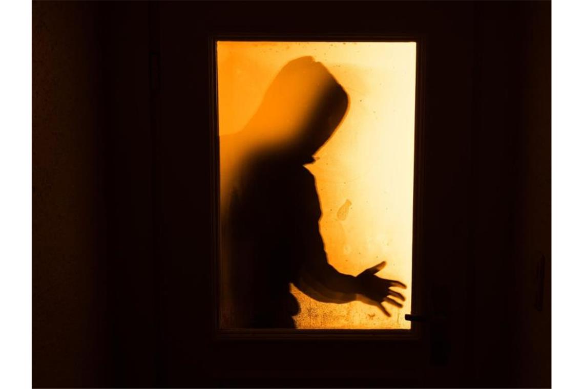 In der Corona-Pandemie wird weniger eingebrochen Der Schatten eines Mannes hinter einer gläsernen Wohnungstür. Foto: Nicolas Armer/Symbolbild/dpa