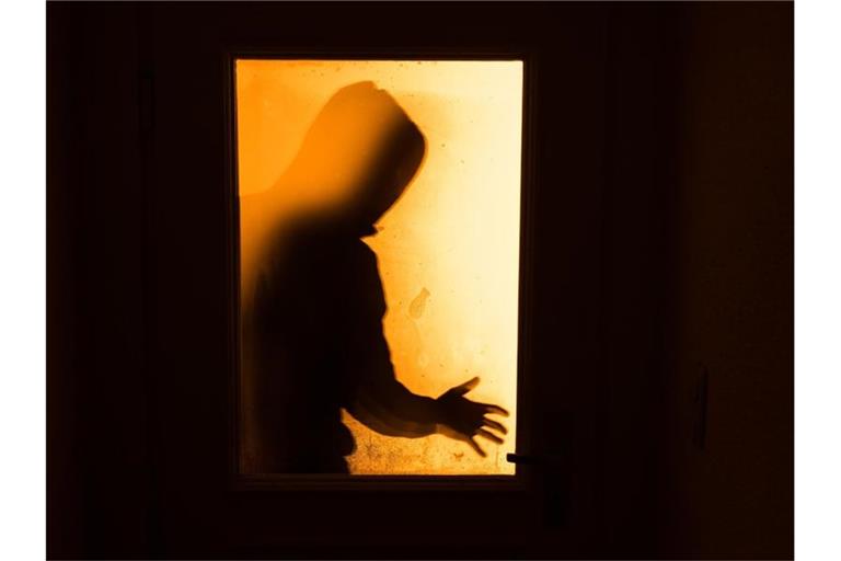 Der Schatten eines Mannes ist hinter einer Glastür zu sehen. Foto: Nicolas Armer/dpa/Symbolbild