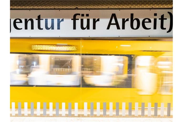 Der Schriftzug "„Agentur für Arbeit“" steht am frühen Morgen an einer Stuttgarter Haltestelle geschrieben, während im Hintergrund eine Stadtbahn einfährt. Foto: Christoph Schmidt/dpa