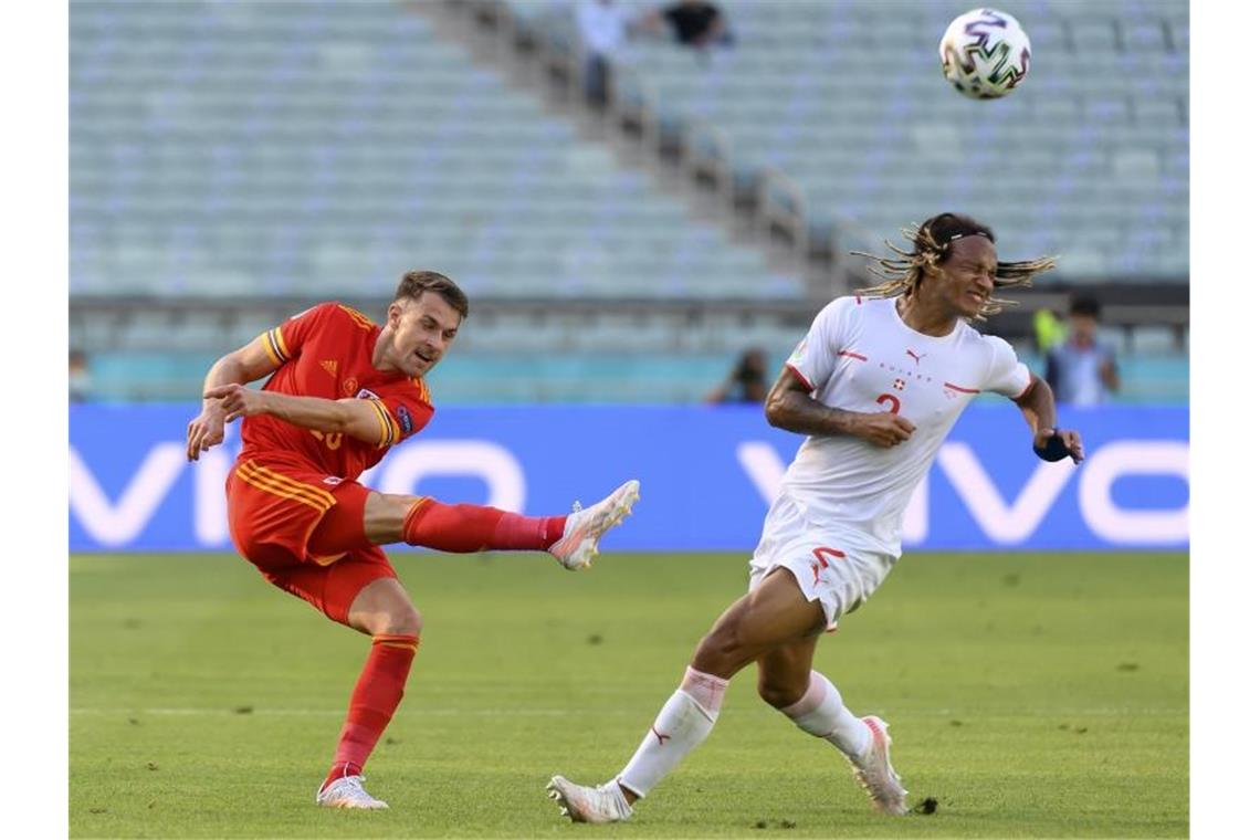 Der Schweizer Kevin Mbabu (r) blockt eine Flanke des Walisers Aaron Ramse. Foto: Jean-Christophe Bott/Keystone/dpa