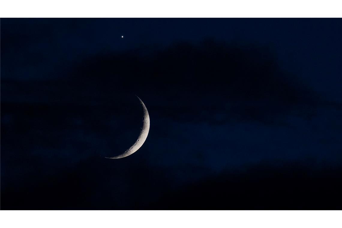 Der sichelförmige Mond wird am Abend hinter Wolken über Köln von der Venus (oben) begleitet.