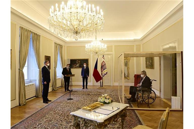 Der tschechische Präsident Milos Zeman (r) sitzt während der Vereidigung von Petr Fiala (l) in einem Rollstuhl hinter einer durchsichtigen Wand. Foto: Roman Vondrous/CTK/AP/dpa
