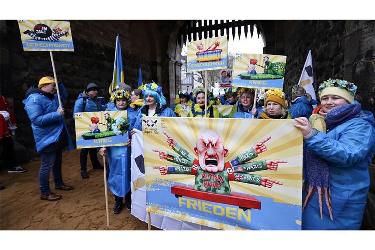 Der ukrainische Hilfsverein Blau-Gelbes-Kreuz hält Plakate mit Putin-Motiven hoch. Das ist als Zeichen der Solidarität mit Wagenbauer Jacques Tilly gemeint. Dieser wird in Russland strafrechtlich verfolgt.