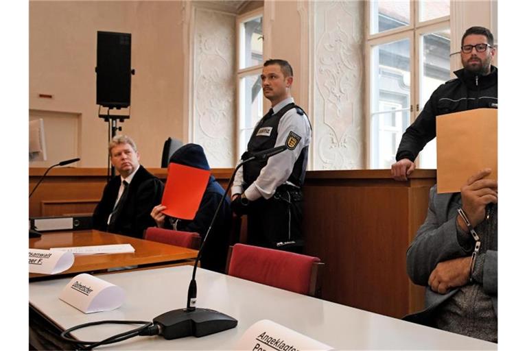Der Vater (r) auf der Anklagebank mit Aktendeckel vor dem Gesicht, links einer der angeklagten Söhne. Foto: Stefan Puchner/dpa/Archivbild