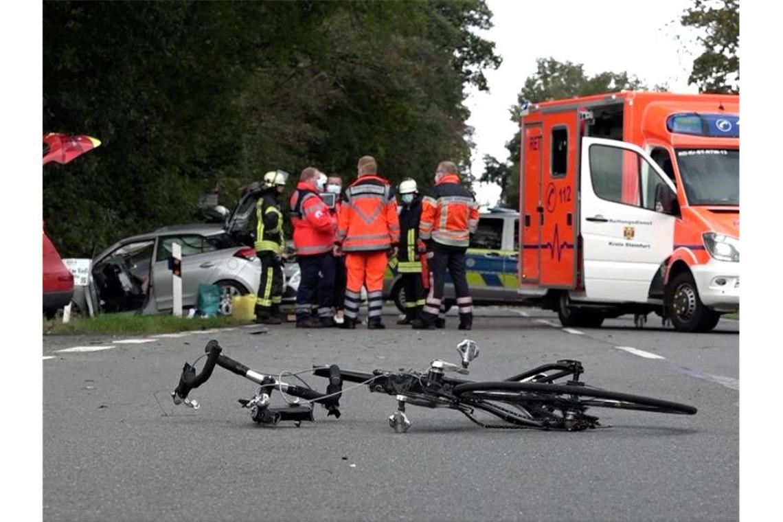 Der zerbrochene Rahmen eines Rennrads liegt an der Unfallstelle in Lienen. Im Hintergrund stehen Einsatzkräfte von Feuerwehr und Rettungsdienst. Foto: -/Nord-West-Media TV/dpa