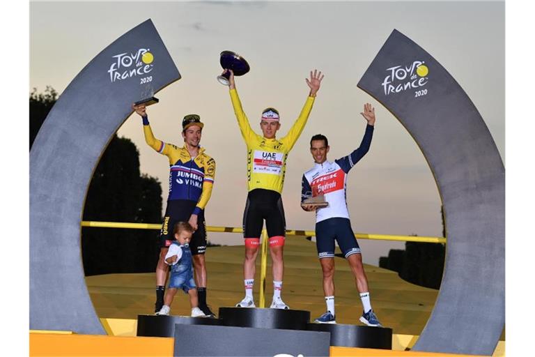 Der Zweitplatzierte Primoz Roglic (l-r) (mit seinem Sohn Lev), Tour-Sieger Tadej Pogacar und der Drittplatzierte Richie Porte feiern auf dem Podium. Foto: David Stockman/BELGA/dpa