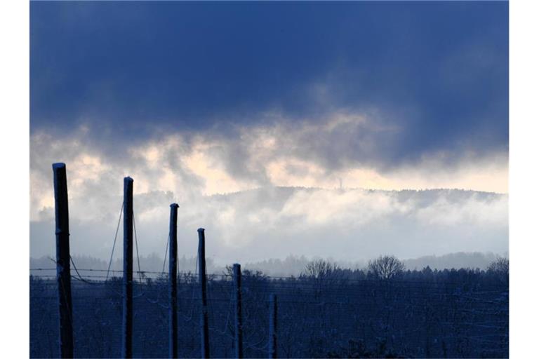 Dichte Wolken bedecken den Himmel, während im Hintergrund ein Sendemast auf einem Berg zu sehen ist. Foto: Felix Kästle/dpa/Archivbild