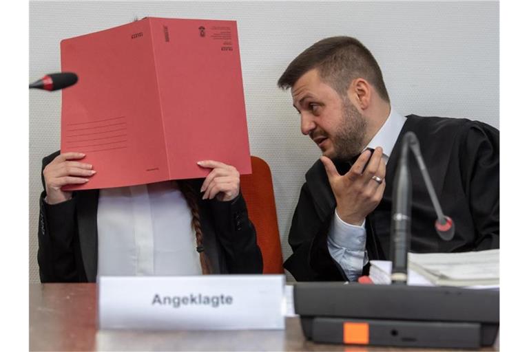 Die Angeklagte Jennifer W. hält im Gerichtssaal einen roten Aktendeckel vor das Gesicht. Rechts neben ihr sitzt Anwalt Ali Aydin. Foto: Peter Kneffel/dpa