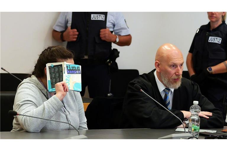 Die Angeklagte (l) sitzt vor der Urteilsverkündung im Verhandlungssaal des Landgerichts Heidelberg und verdeckt ihr Gesicht.