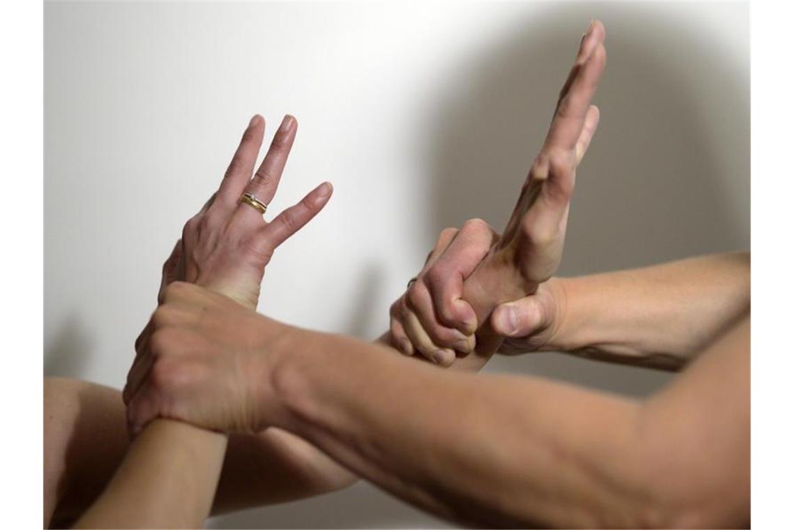 Die Arme eines Mannes (r) halten mit Gewalt die Arme einer Frau fest. Foto: Maurizio Gambarini/dpa/Symbolbild
