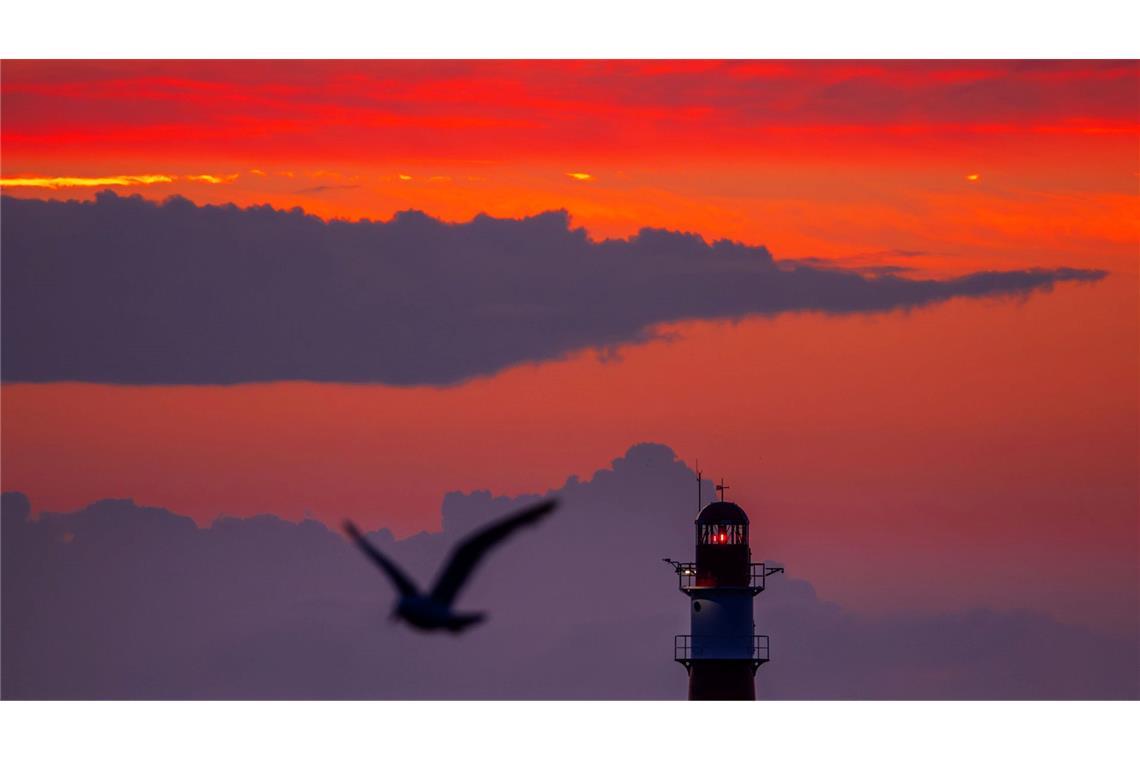 Bilder des Tages Die aufgehende Sonne färbt den Himmel hinter dem Leuchtfeuer auf der Ostmole am Ostseestrand von Warnemünde orangerot.