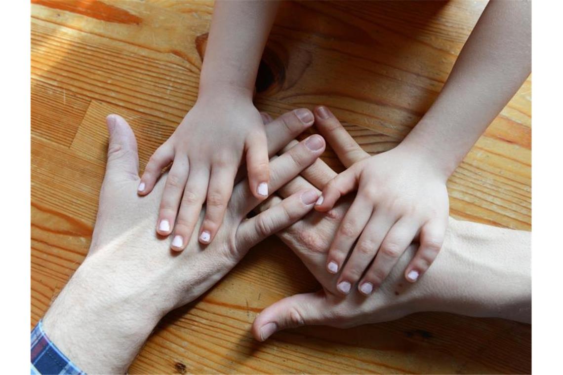 Zahl der Adoptionen im Südwesten auf Rekordtief Die Hände eines Paares und eines Kindes liegen auf einem Tisch (gestellte Szene). Foto: Jens Kalaene/Archivbild