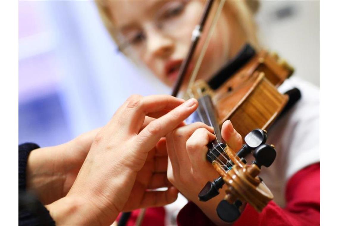 Die Hand einer Musikschülerin wird von der Musiklehrerin beim Geigespiel korrigiert. Foto: Jens Büttner/dpa-Zentralbild/dpa/Archivbild