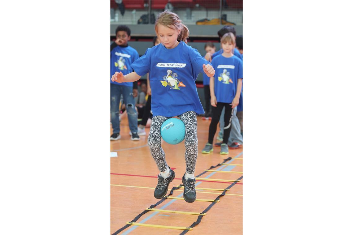 Die Känguru-Station: mit dem Ball zwischen der Oberschenkeln springen die Schüler durch die Felder der Koordinationsleiter.